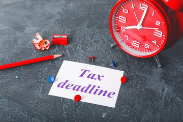 Paper with text TAX DEADLINE, alarm clock and pencil on dark table