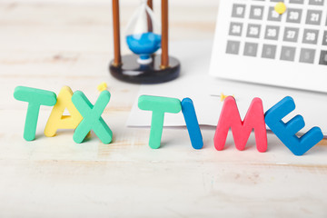 Text TAX TIME, calendar and hourglass on table