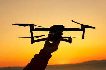 Silhouette of hand launching professional drone into the air at low altitude blue sky background and orange sunset in mountains. Solar disk. Drone takes pictures. Modern new technologies