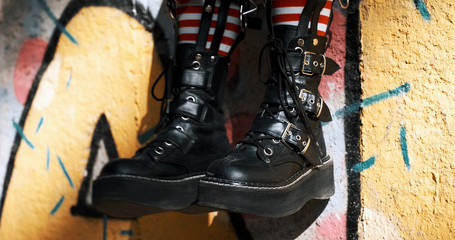 Goth teenager girl slide with rough boots striped stockings sits on ornate wall of an abandoned building. Alternative in youth. An alternative in youth. Hipster, freak, emo, grunge. Copy 