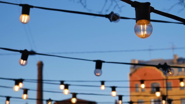 Lanterns in the evening against the background of the sunset, dark blue sky. Light bulbs against the background of wires and blue sky, pleasant warm yellow light.