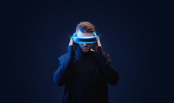 Model young man with beard in glasses of virtual reality on dark background. Augmented reality, future technology concept. VR. Blue neon light.