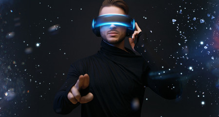 Guy using VR helmet scrolling invisible screen while interacting with virtual reality under blue neon light. Augmented reality, future technology, game concept.