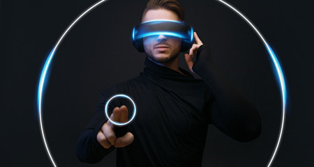 Guy using VR helmet scrolling invisible screen while interacting with virtual reality. Blue neon...