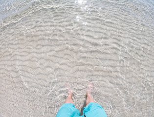 Male Feet standing on the shallow crystal Sea Water Beach Sand. Concept of relsx and happiness.