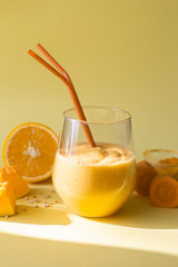 Diet healthy vegetarian smoothie made of pumpkin, carrot, orange, nuts and green sprouted buckwheat in a glass glass on a yellow background in the rays of bright hard sunlight.
