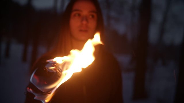 Young woman standing outdoors at night with a fire torch and looking around