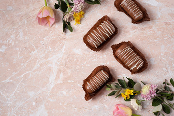 Chocolate pop cake with spring delicate flowers on a pink marble background. Top view, horizontal image of copy space