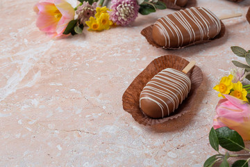 Chocolate pop cake with spring delicate flowers on a pink marble background. Top view, horizontal image of copy space.