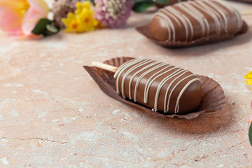 Chocolate pop cake with spring delicate flowers on a pink marble background. Top view, horizontal image of copy space