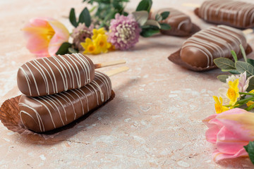 Chocolate pop cake with spring delicate flowers on a pink marble background. Top view, horizontal image of copy space