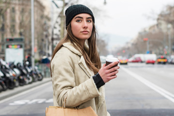Portrait of young european woman walking in a city street, with takeaway coffee in hands