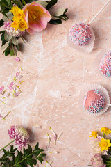 Fototapeta na wymiar Spring frame copy space from early spring flowers and bright pink cake pops on a pink marble background.