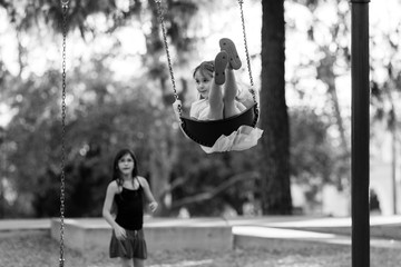 An older sister is pushing her younger sister on a swing in black and white.