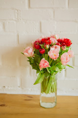 Glass vase with bouquet of beautiful tulips on brick wall background
