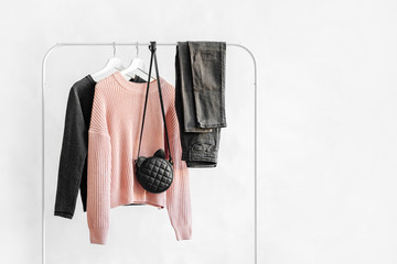 Female clothes in pastel pink and gray color on hanger on white background.  Jumper, shirt, jeans...