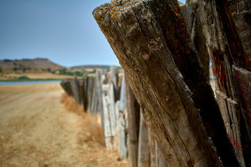 foreground detail of a deteriorated agricultural fencing with a lagoon and unfocused hills in the...