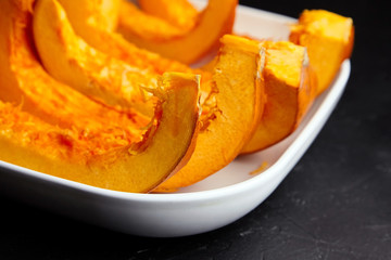 Slices of uncooked pumpkin in white ceramic plate on black background