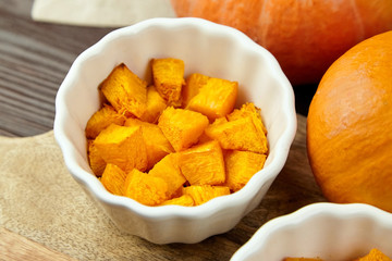 Pieces of baked pumpkin in white ceramic bowl on wooden background