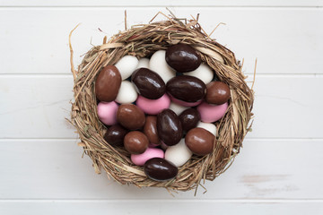 Top view of bird nest with chocolate and sweet easter eggs on white wooden table