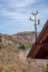 Meteorological station placed on a wooden roof. At the back, a mountain with foliage and a semi...