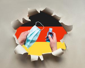 Germany fights against coronavirus. Hands with face mask and disinfection gel in paper hole with...