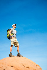 Fototapeta premium Hiker standing outdoors on the top of a red rock mountain under sunny blue sky