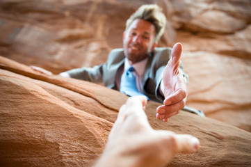 Businessman holding out helping hand to pull someone up from red rock canyon