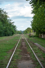 Fototapeta premium An abandoned railway track surrounded by plants with a person on a horse at the very back