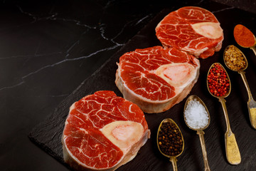 Raw cross cut beef shank and seasonings on black board.