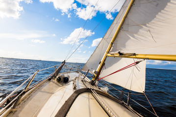 Sloop rigged yacht sailing on a clear day. A view from the deck to the bow and sails. Waves and...