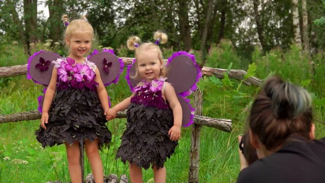 Female photographer takes pictures of beautiful girls playing violet butterflies. Girls wear handmade butterfly wings