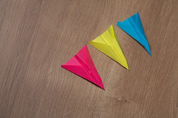 Three colorful handmade paper airplanes in a row resting on a wooden surface