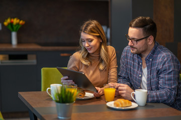 Happy couple using tablet and having breakfast in the kitchen