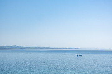 Minimalist landscape - lonely fishing boat in the vast ocean in bright sunlight under blue sky with copy space