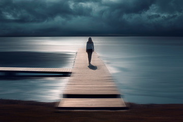 Woman walks on wooden pier at sea. Artistic blur effect used.