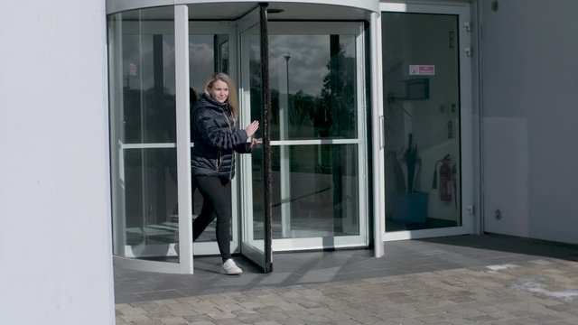 Female employee leaves office building through a revolving door after work.