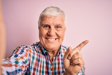 Senior handsome hoary man wearing casual shirt making selfie by the camera very happy pointing with hand and finger to the side