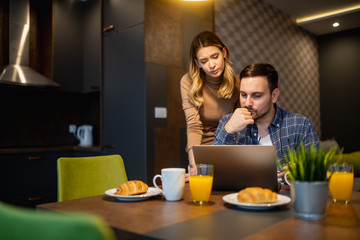 Happy couple using tablet and having breakfast in the kitchen