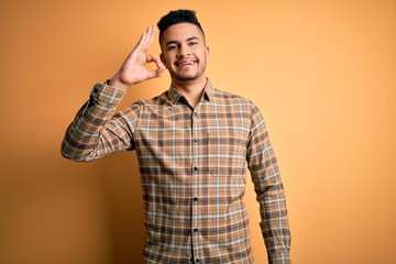 Young handsome man wearing casual shirt standing over isolated yellow background smiling positive doing ok sign with hand and fingers. Successful expression.