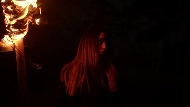 Young woman holding fire torch walking in dark forest at night