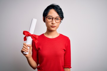 Beautiful chinese student woman wearing glasses holding university graduated diploma degree with a confident expression on smart face thinking serious