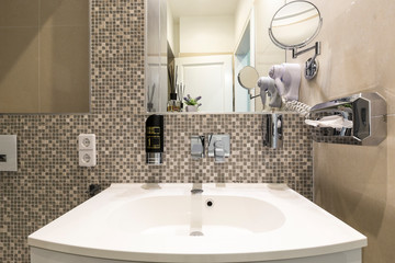 Close up of luxurious white sink in upscale bathroom of European vacation apartment or hotel suite interior, equipped with several accessories