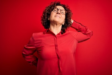 Middle age beautiful curly hair woman wearing casual shirt and glasses over red background Suffering of neck ache injury, touching neck with hand, muscular pain