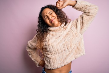 Young beautiful woman with curly hair wearing casual sweater standing over pink background stretching back, tired and relaxed, sleepy and yawning for early morning