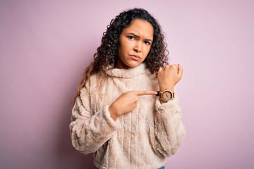 Young beautiful woman with curly hair wearing casual sweater standing over pink background In hurry...