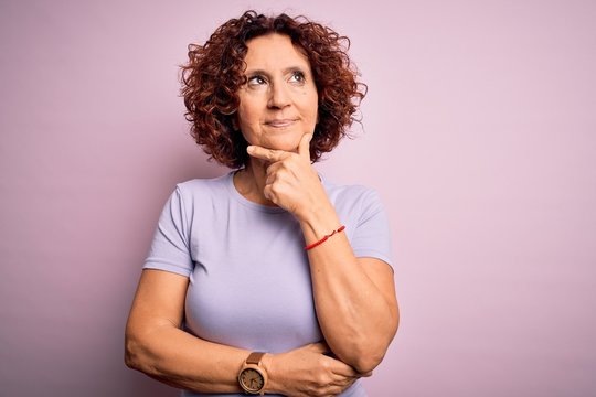 Middle Age Beautiful Curly Hair Woman Wearing Casual T-shirt Over Isolated Pink Background With Hand On Chin Thinking About Question, Pensive Expression. Smiling With Thoughtful Face. Doubt Concept.