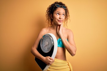 Young beautiful american slim woman on vacation wearing bikini holding weight machine serious face...