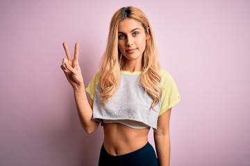 Young beautiful blonde sporty woman doing sport wearing sportswear over pink background smiling...
