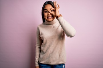 Young beautiful asian girl wearing casual turtleneck sweater over isolated pink background doing ok gesture with hand smiling, eye looking through fingers with happy face.